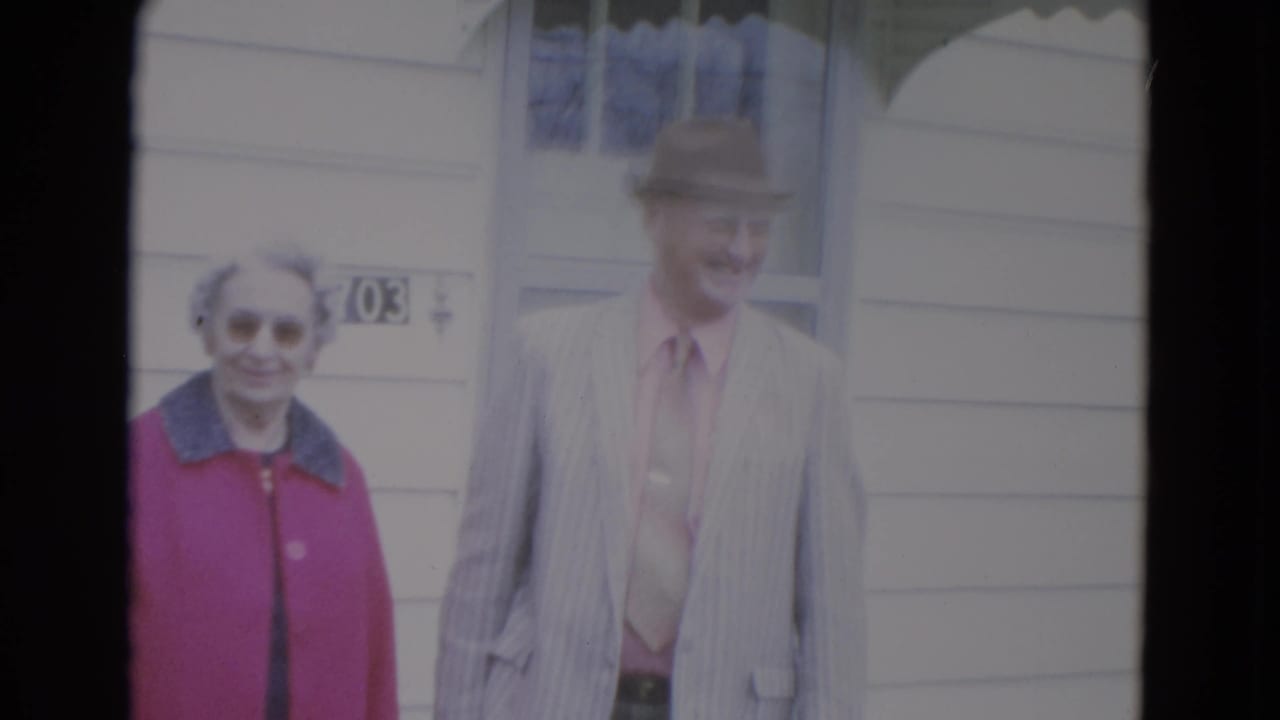 Elderly woman and man standing outside a white-sided house.