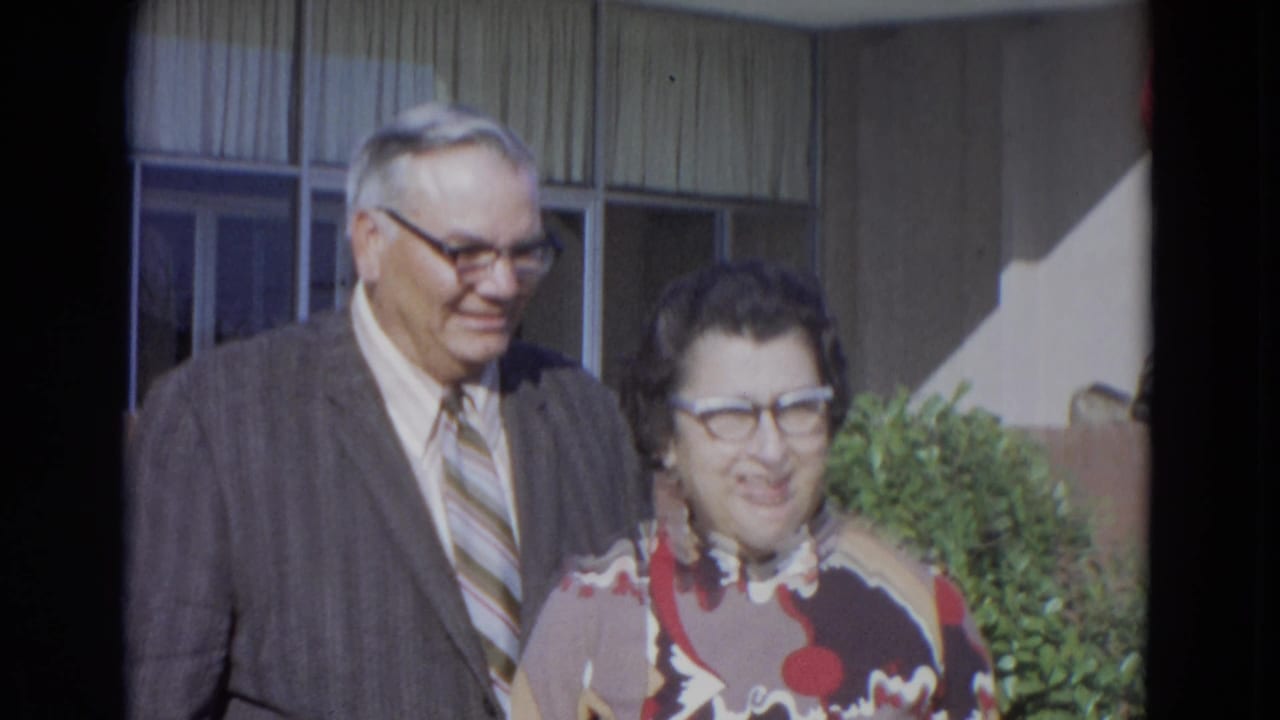Middle-aged couple standing outside a building and smiling toward the camera.