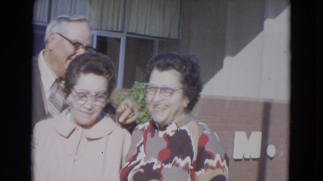 Man and two women smiling outside a building with brickwork and windows.