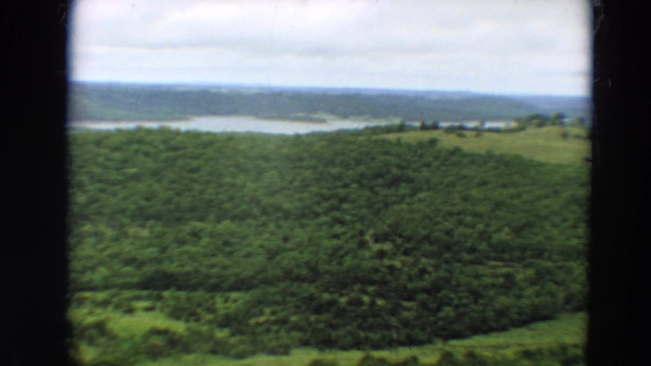 1967 Minnesota 8mm frame showing forested hills and a calm distant river or lake under overcast sky.