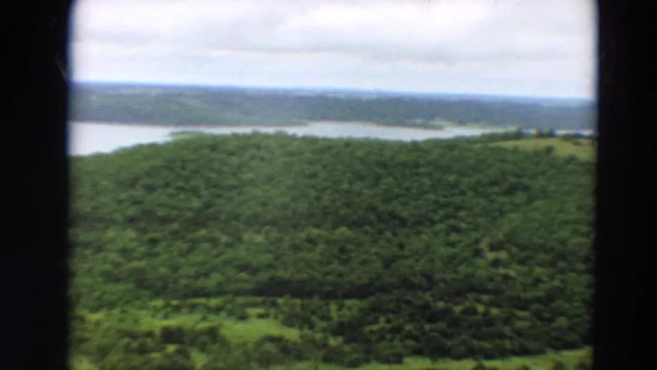 Soft 8mm view of Minnesota woodland with a wide calm waterway and distant tree line under clouds.
