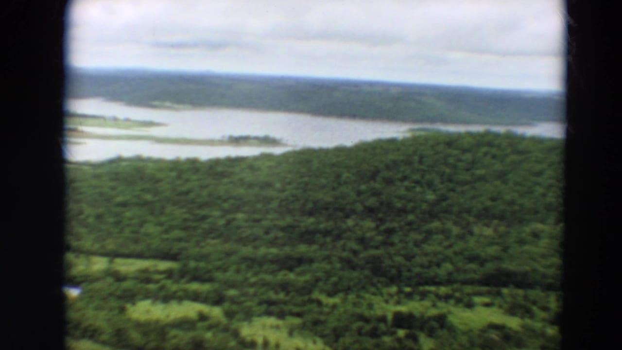 Aerial view over wooded hills and broad water under a cloudy sky.