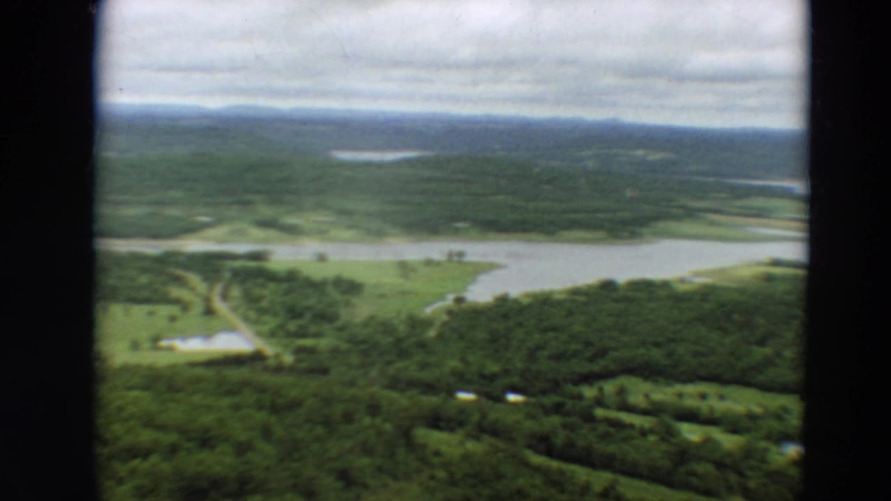 Aerial view of wooded terrain, waterways, fields, and a narrow road or track.