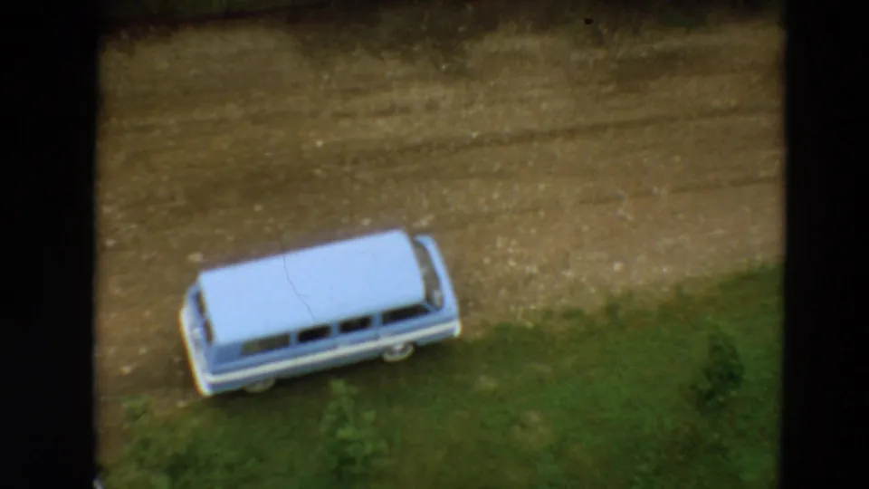 Light blue 1960s-style station wagon parked on a dirt road in a Minnesota yard setting, filmed from above on 8mm.