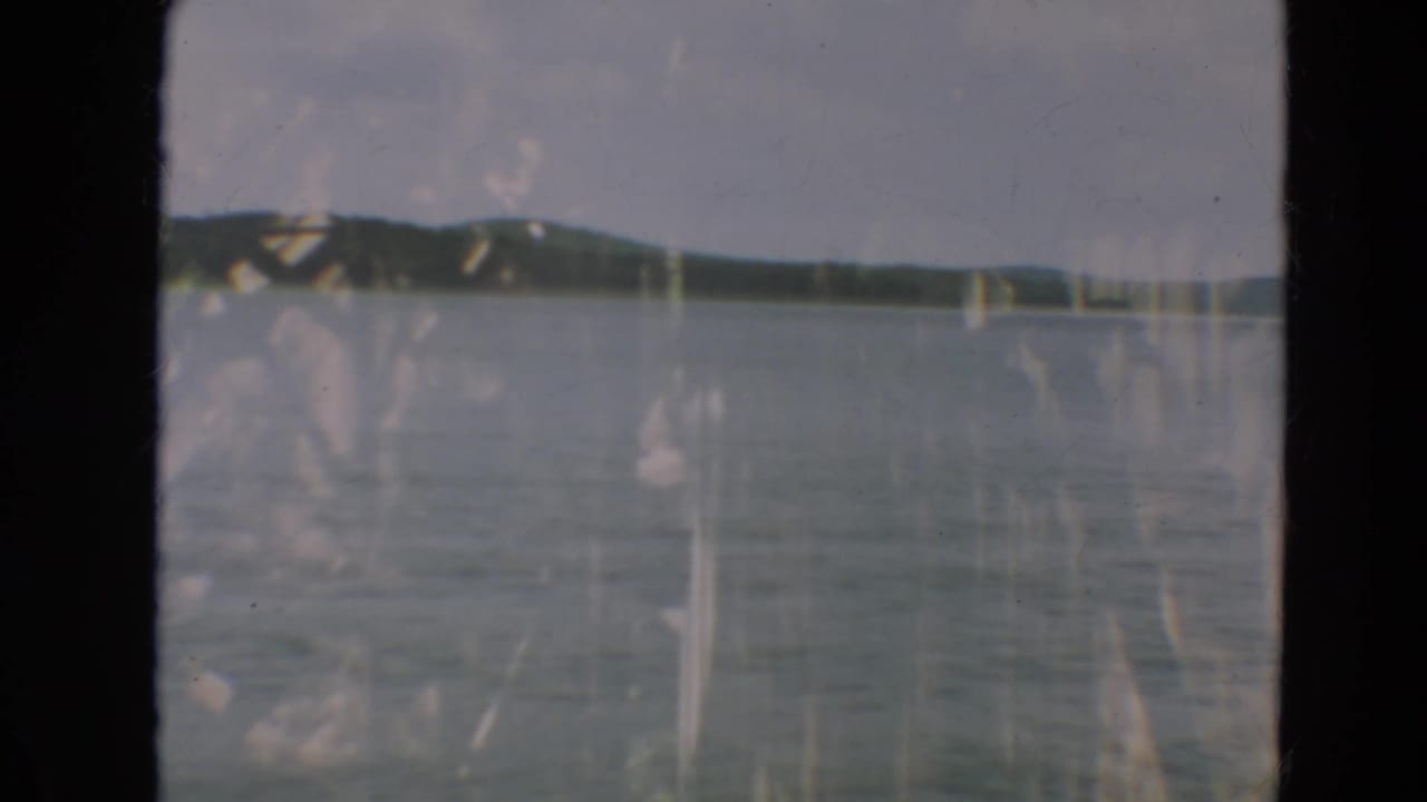 Calm lake with distant wooded hills under a pale sky, seen through dark 8mm frame borders.