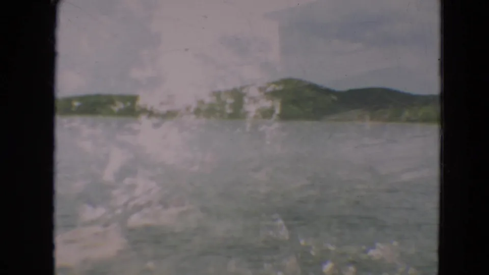 1967 Minnesota 8mm view of a lake and far shoreline, partly obscured by scratches, haze, and window or film marks.
