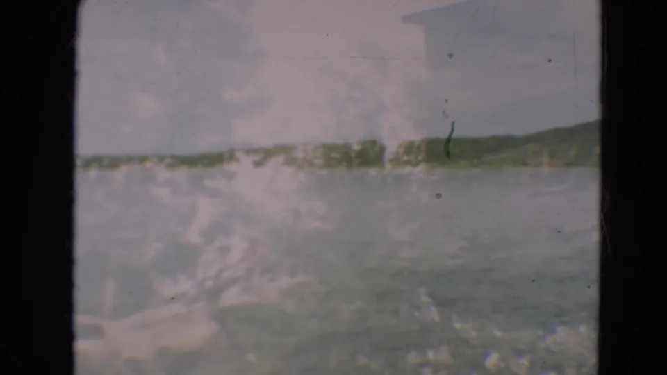 1967 Minnesota 8mm frame with a distant lake horizon, wooded landforms, bright glare, and visible film scratches.