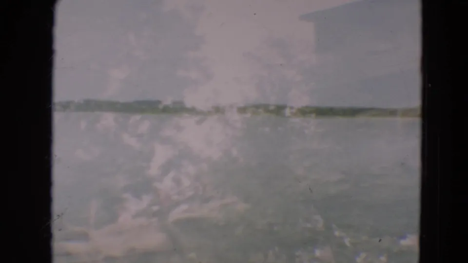 1967 8mm frame from Minnesota showing a soft, faded lakeside view with water, distant shore, and heavy film gate borders.
