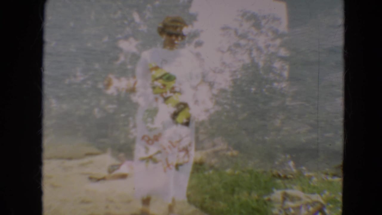 Woman in sunglasses standing near lake water in a white bumblebee dress.