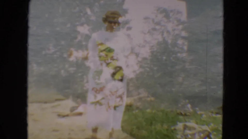 Woman in sunglasses stands near a Minnesota lakeside in 1967, wearing a white dress with a large bumblebee graphic.