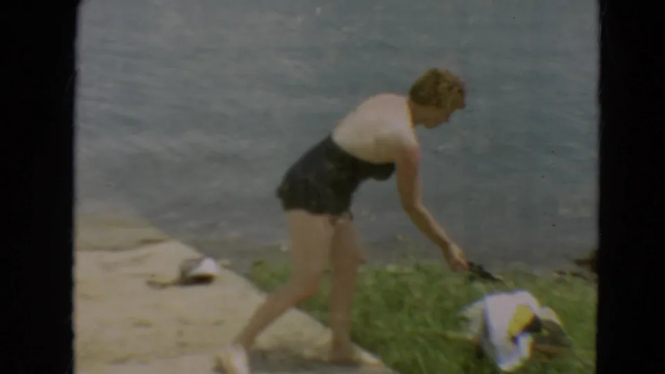 The woman bends near personal items on the grass and concrete beside the Minnesota lakeshore.
