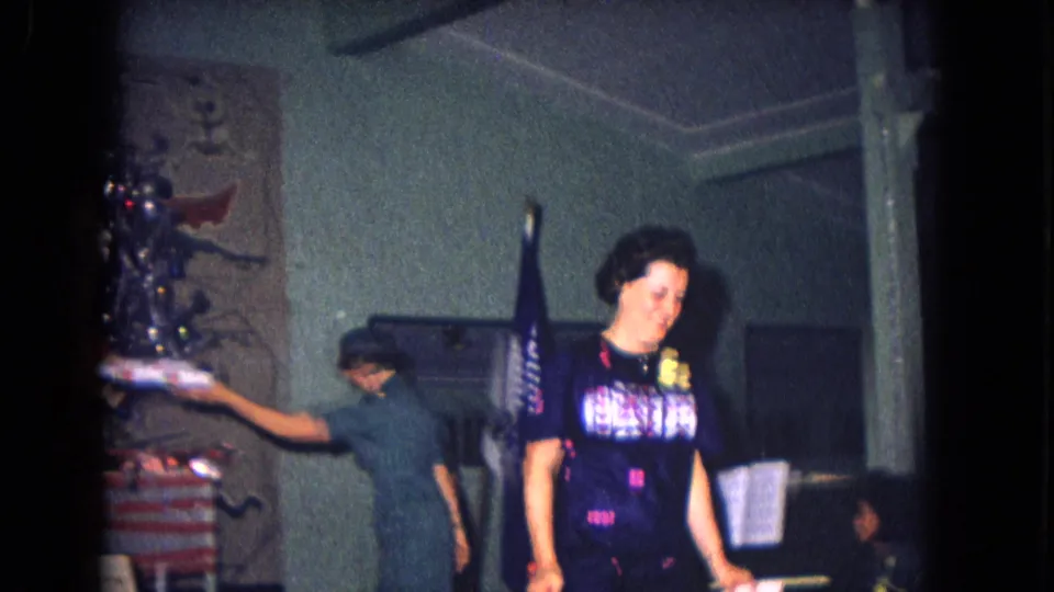 A 1967 New Mexico holiday gathering frame shows an adult leaving the tree area as another person works near the table.