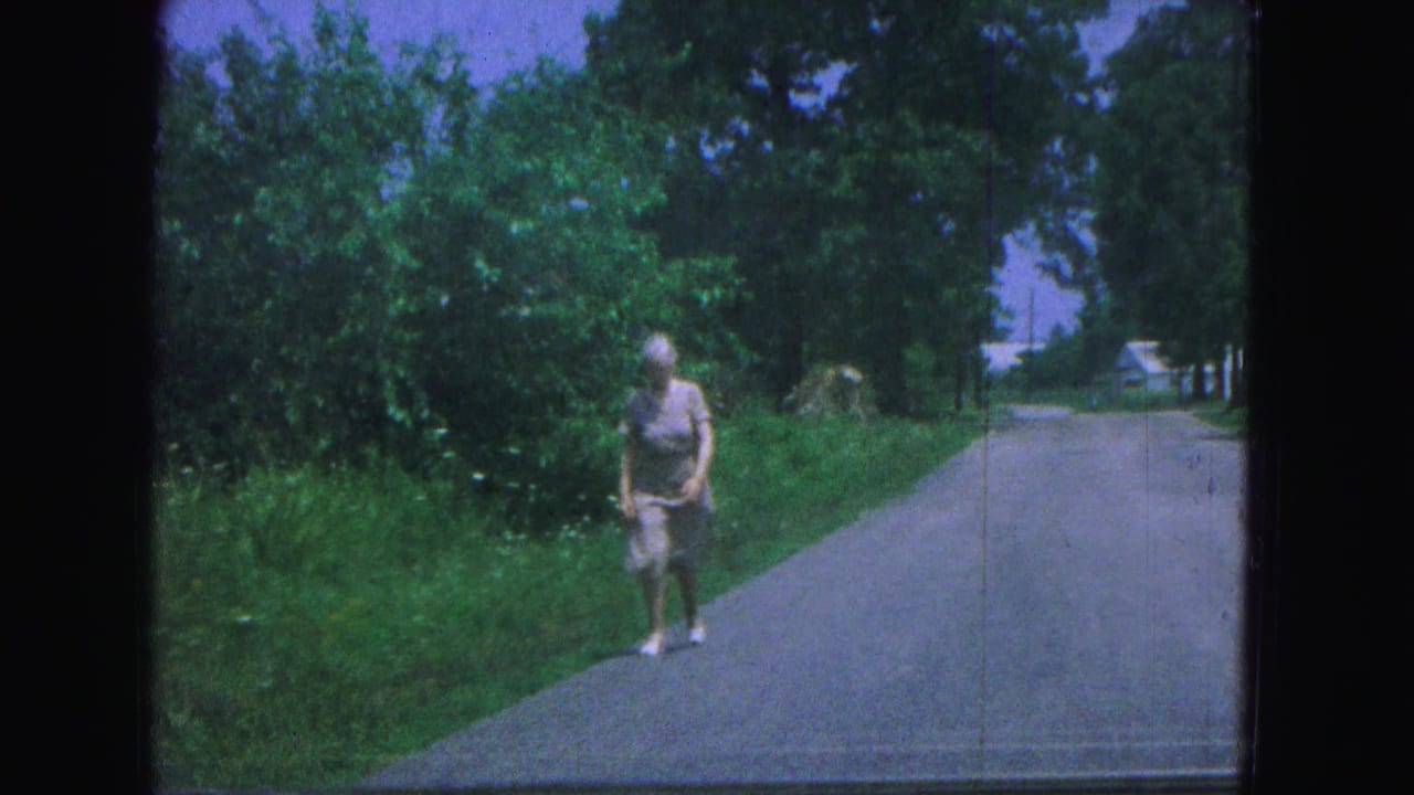 Woman walking along a paved rural road bordered by trees and grass.