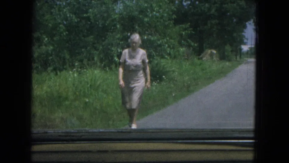 The final frame shows the woman near the road edge, with dense trees and grass behind her in a 1967 New Mexico home movie.