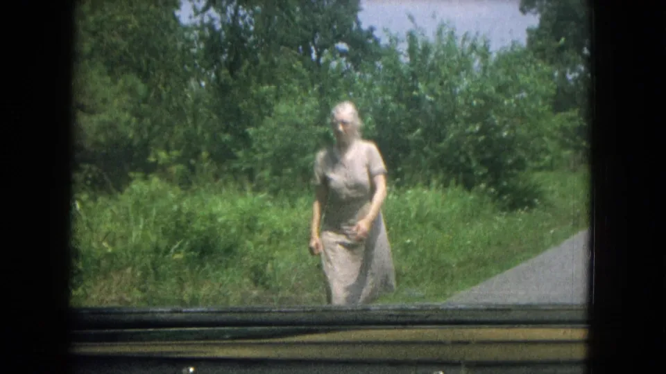 Near the end of the 1967 New Mexico clip, the elderly woman is close to the car-window camera beside the rural driveway.