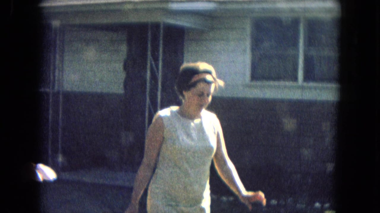 Woman in a light sleeveless dress walks outdoors beside a residential building.