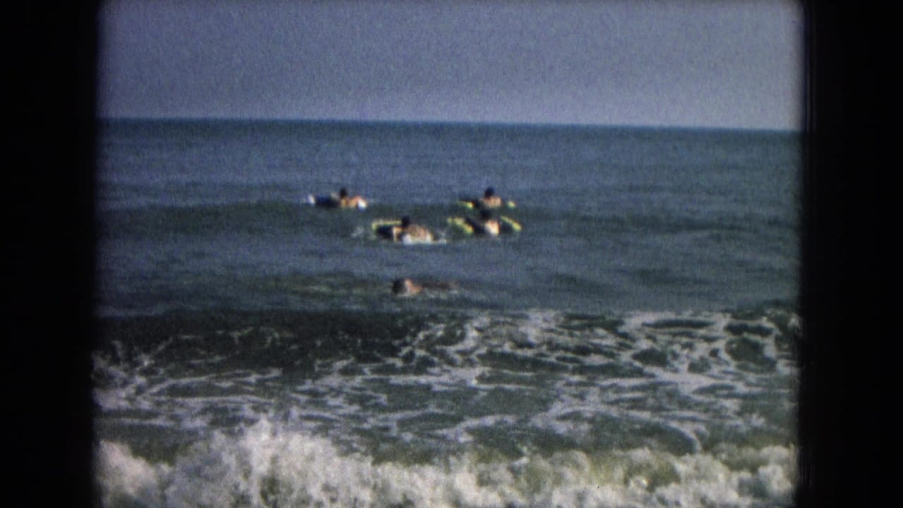 1960s 8mm home-movie frame of people in swimwear using inflatable tubes and swimming in low surf.