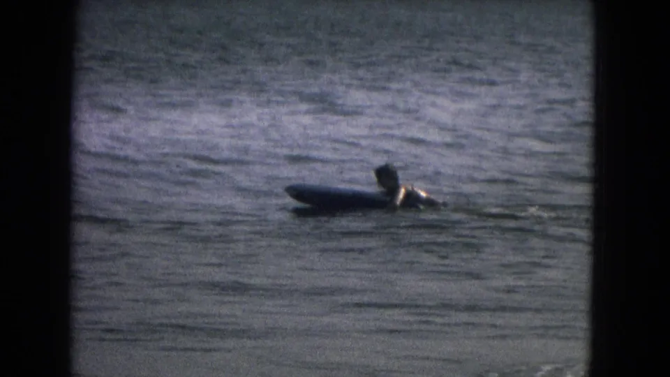 The swimmer or surfer remains beside a thick board in calm water, framed by dark 8mm contact-sheet edges.