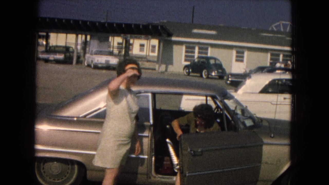 Woman beside a classic sedan while another person sits in the open front seat.