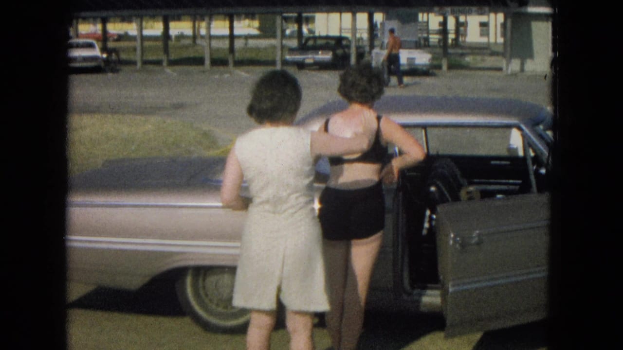 Two women stand beside an open car door in a sunny parking area.