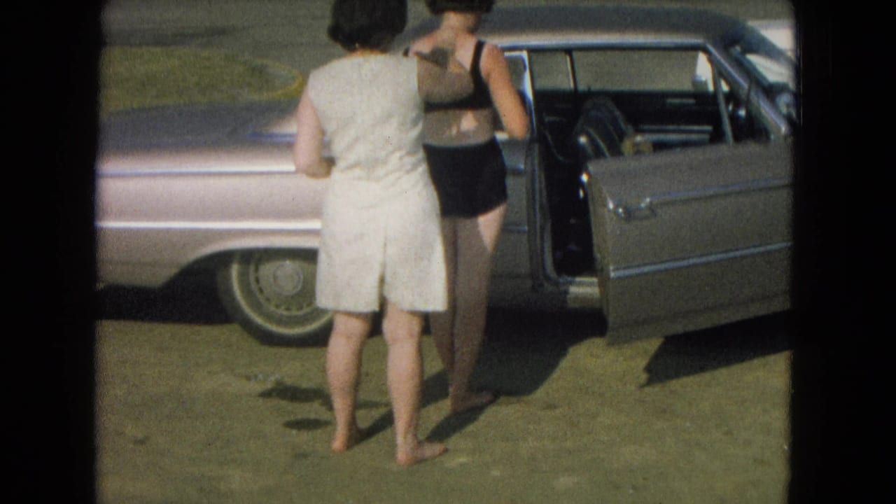 Two women stand close together beside a car with its door open.