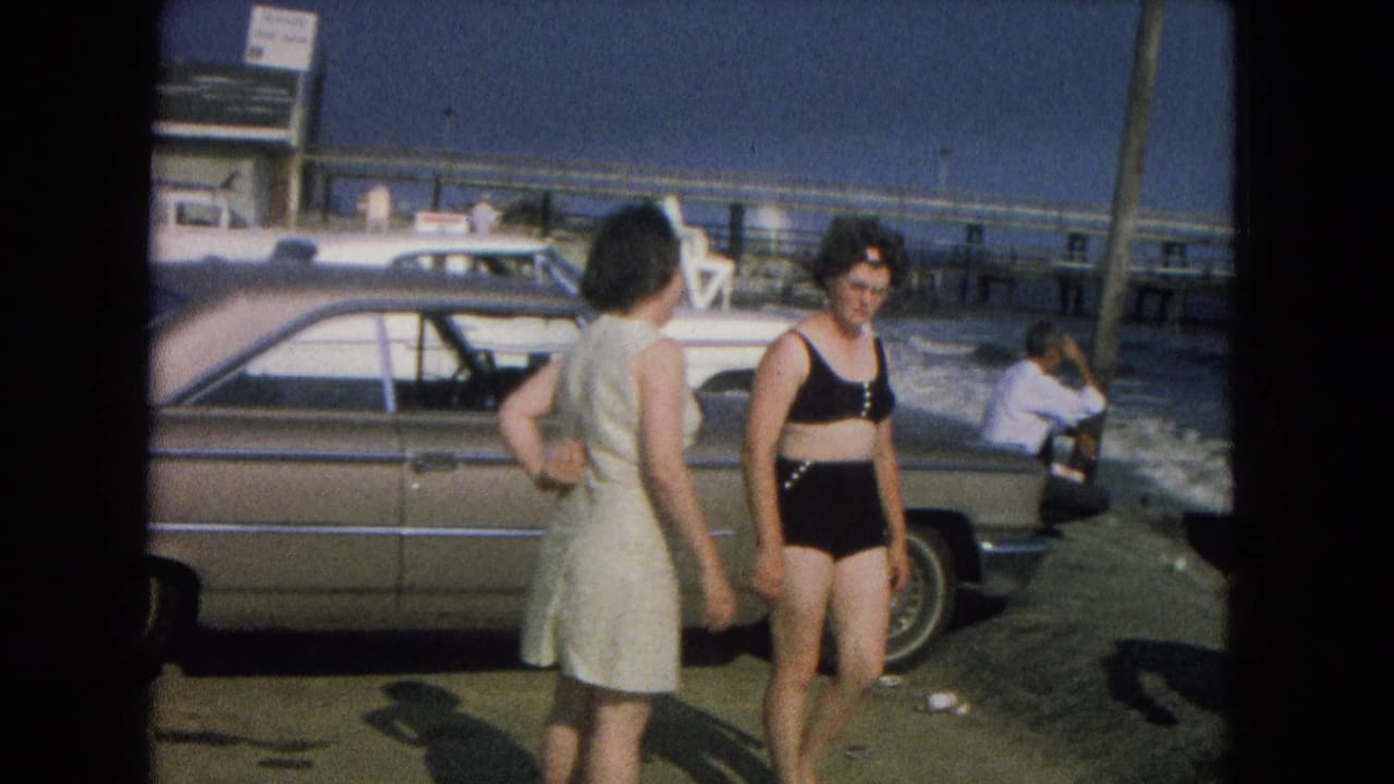 Woman in black bikini walks beside a parked sedan near the surf.