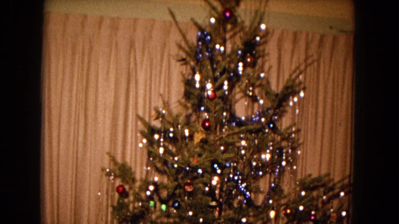 1967 New Mexico home-movie frame showing a lit Christmas tree with ornaments, tinsel, and a star topper before pale curtains.