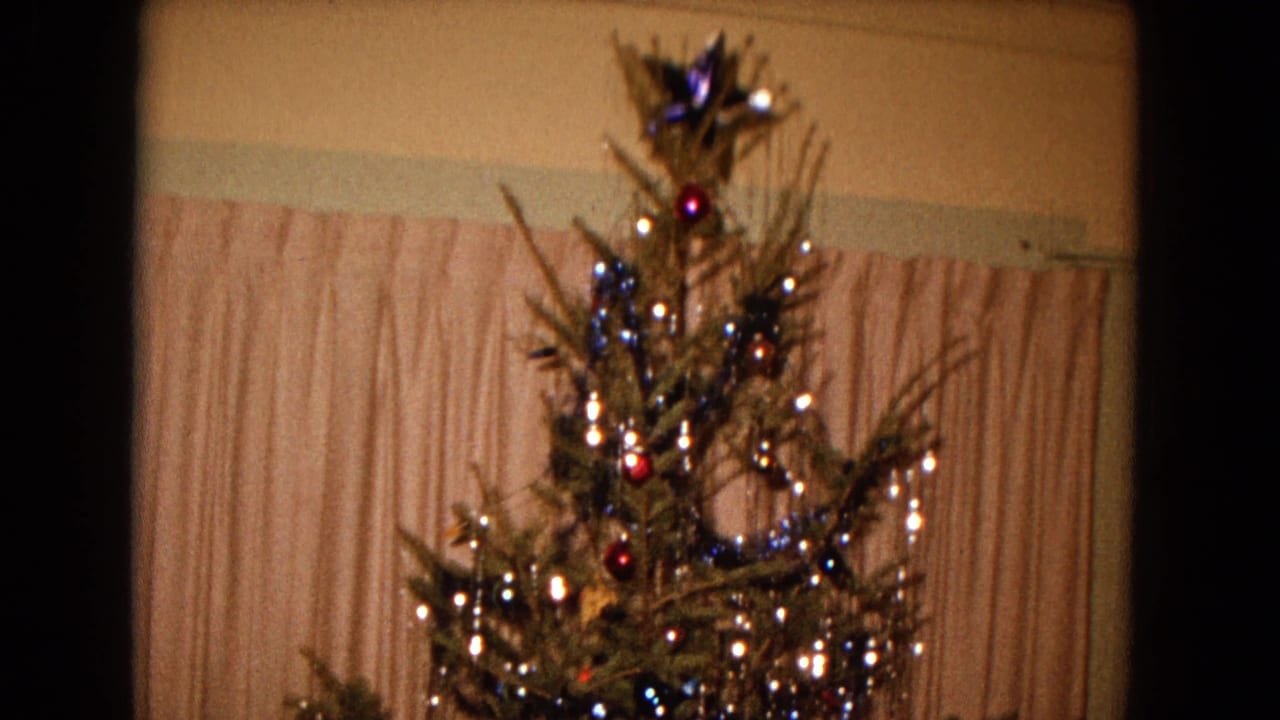 Christmas tree top with ornaments, lights, tinsel, and curtain backdrop.
