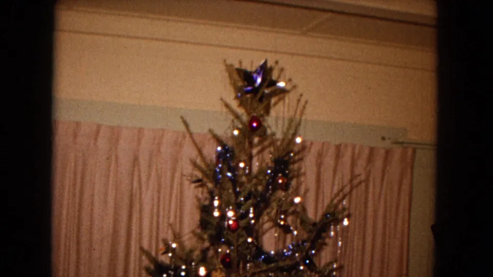 A slightly tilted 8mm frame shows the Christmas tree top, ornaments, lights, and curtained wall inside the 1967 New Mexico home.