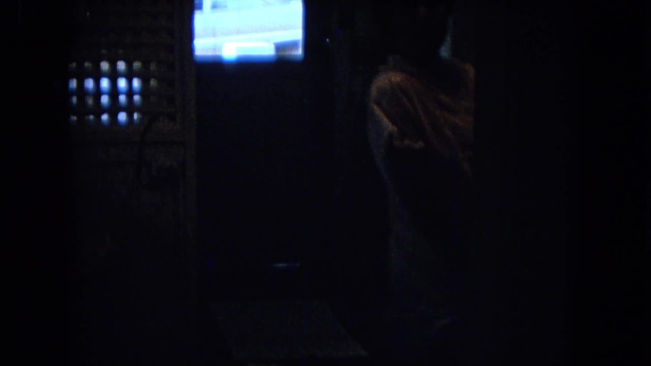 Low-light 1967 New Mexico 8mm frame showing a person in silhouette inside a kitchen, with a bright window and exterior car shape beyond.