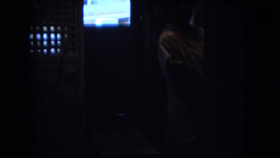Low-light 1967 New Mexico 8mm frame showing a person in silhouette inside a kitchen, with a bright window and exterior car shape beyond.