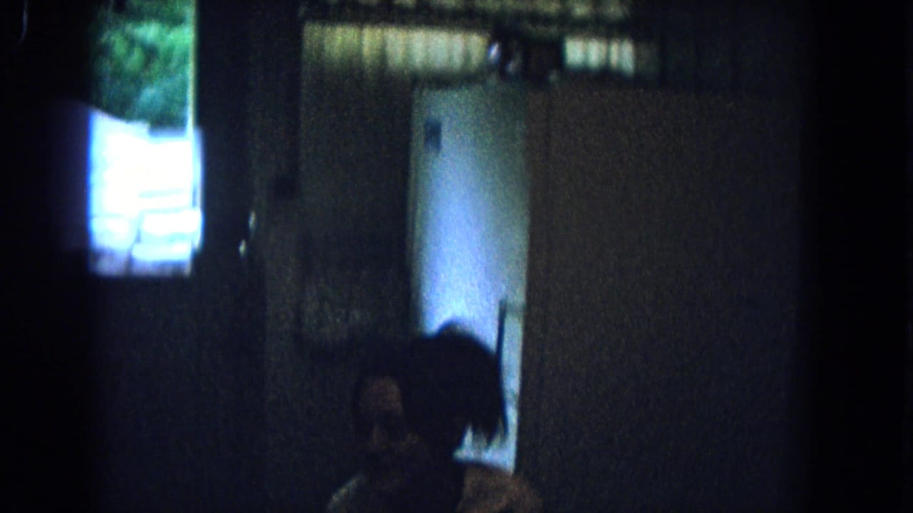 Dark kitchen doorway with a seated or crouched figure near the right side.