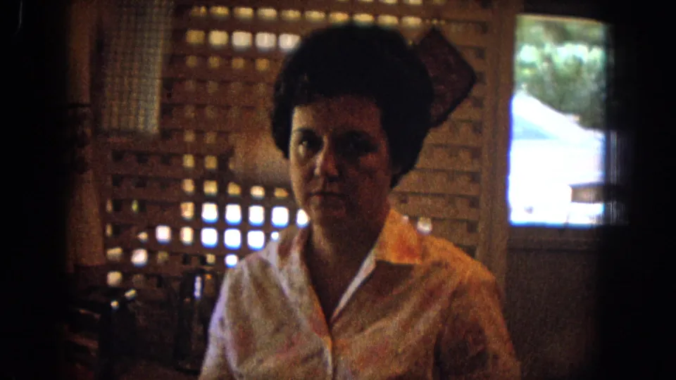 The woman faces the camera in a 1967 New Mexico kitchen, framed by a lattice partition and bright window opening.