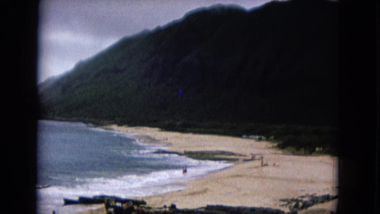 Coastal beach and surf seen from above with mountains behind the shore.