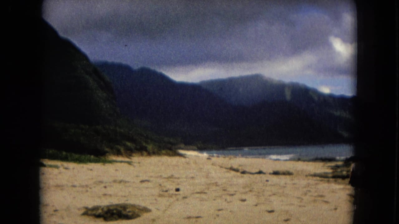 Sandy shore leading toward water and dark mountains under a cloudy sky.