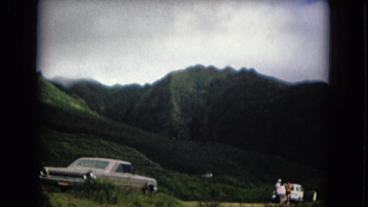 Two parked cars below green mountains with small people near one vehicle.