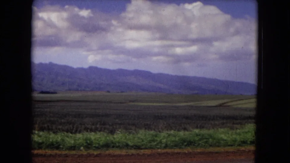 1967 New Mexico landscape frame with broad fields, low vegetation, purple-toned mountains, and heavy cloud cover during a handheld pan.