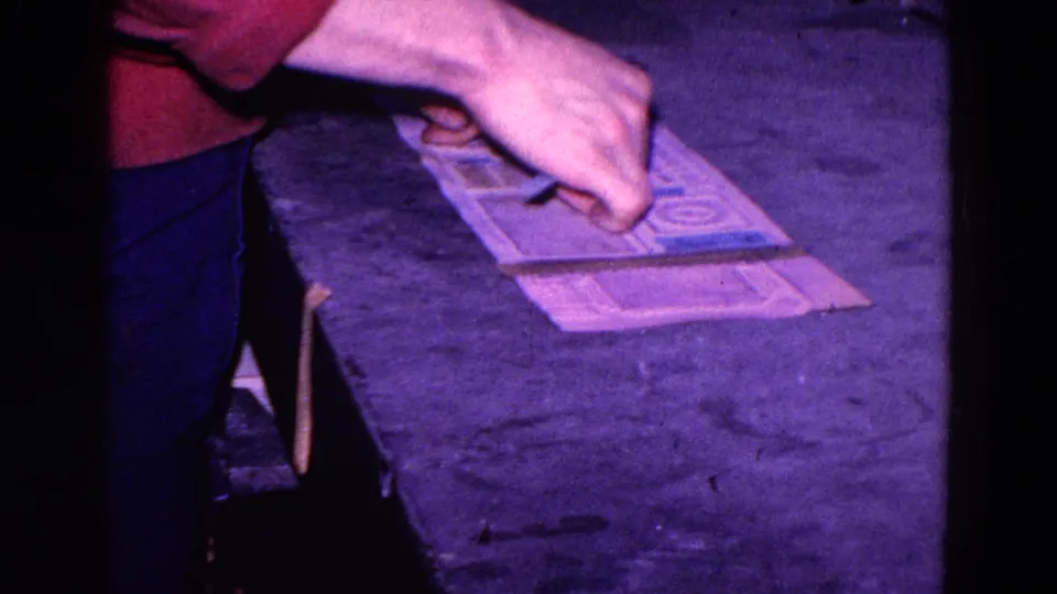 Close 8mm view of hands aligning a paper cutout over another sheet during a 1967 pattern-making activity in Trenton.