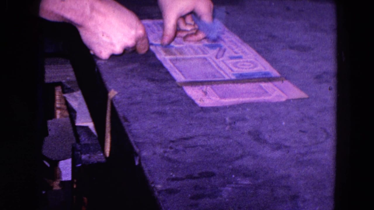 Hands place blue stickers on a printed paper sheet at a dark workbench.