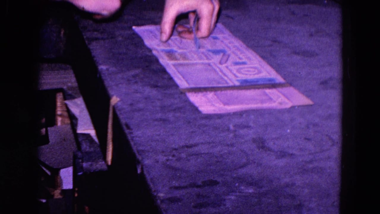 A close view shows hands arranging blue stickers on a printed paper sheet in the Trenton factory setting.