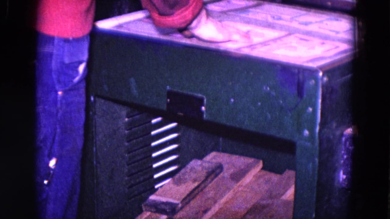 A partial worker in red and blue clothing stands beside a green forge machine in 1967 Trenton workshop footage.