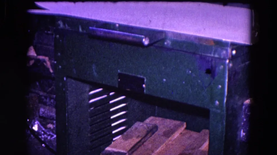Green metal forge or shop machine fills the frame, with vented side panels and boards below in Trenton workshop footage.