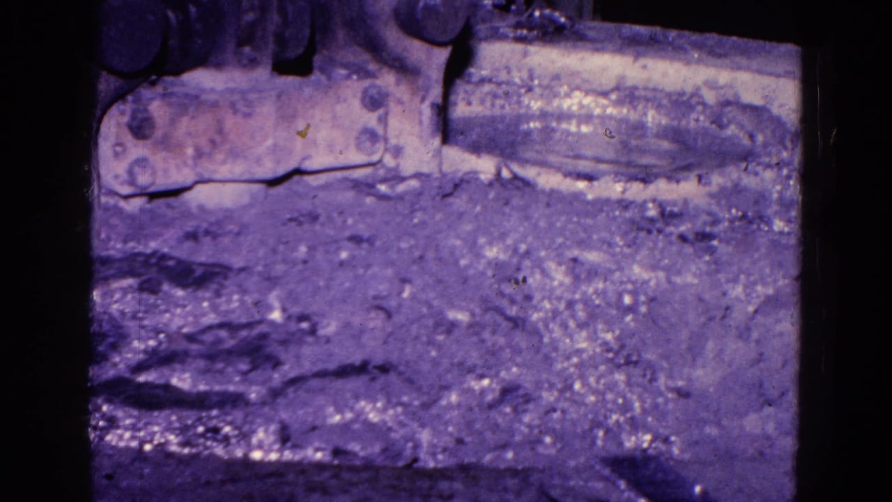 1967 Trenton 8mm frame showing a rough foundry or casting surface beneath dark machine parts, with heavy grain and purple-blue color shift.
