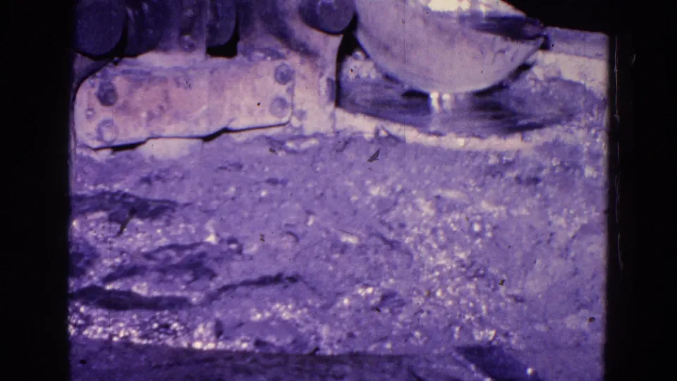 1967 Trenton 8mm frame showing a round machine component over a rough foundry surface, with soft focus, grain, and strong purple color shift.