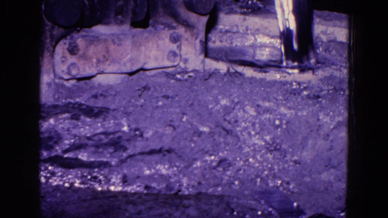1967 Trenton 8mm frame showing rough industrial floor material and metal machinery in low light with heavy purple film cast.