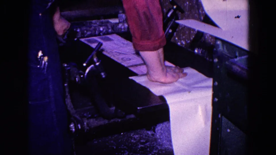 1967 Trenton 8mm frame showing a worker's bare foot on paper with red pants and nearby dark industrial equipment.