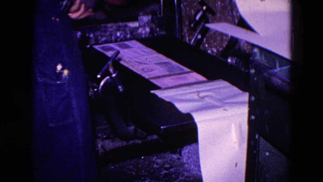 In 1967 Trenton, New Jersey footage, a worker in denim stands near a press with printed sheets feeding across the machine.