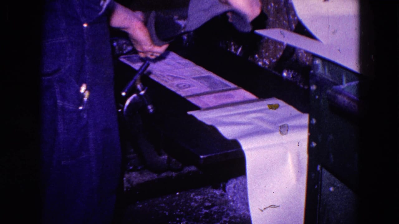 A worker's arm reaches toward paper feeding through a printing press.