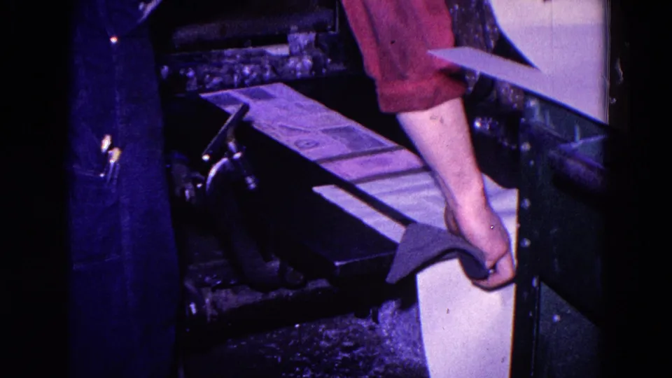 A red-sleeved worker adjusts or gathers paper beside the press during the 1967 Trenton printing process.