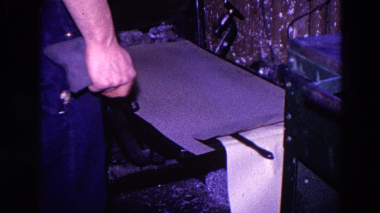 Hands place or wet a sheet of paper near a small metal printing press.